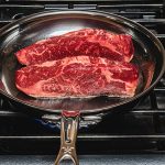 new york strip steaks cooking edge side down